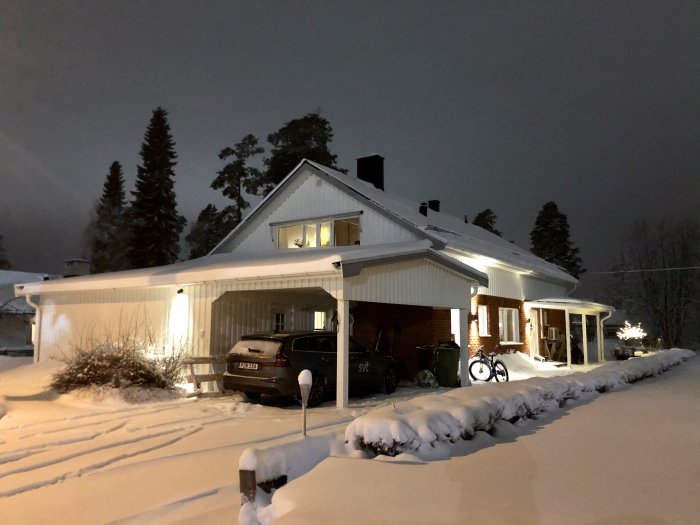 Vit villa med carport i snötäckt landskap belyses av varmt ljus på kvällen