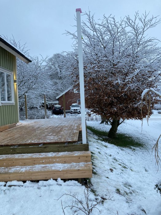 Ny monterad impregnerad limträstolpe vid trätrall med snötäckt trädgård i bakgrunden.