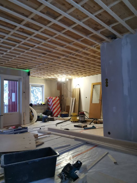 Inomhus byggarbetsplats med pågående installation av träbjälkar i taket och verktyg utspridda på golvet.