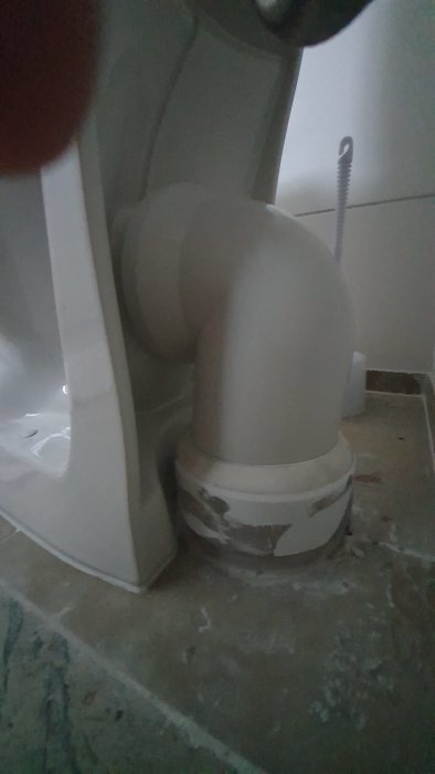 Anslutningen bakom en IFÖ-toalett som visar hur toaletten sticker ut från väggen, med synligt rör i golvet.