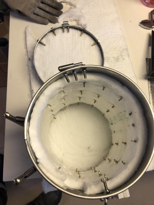 Inre vy av en rostfri behållare isolerad med vit fiberisolering och fästplåtar.