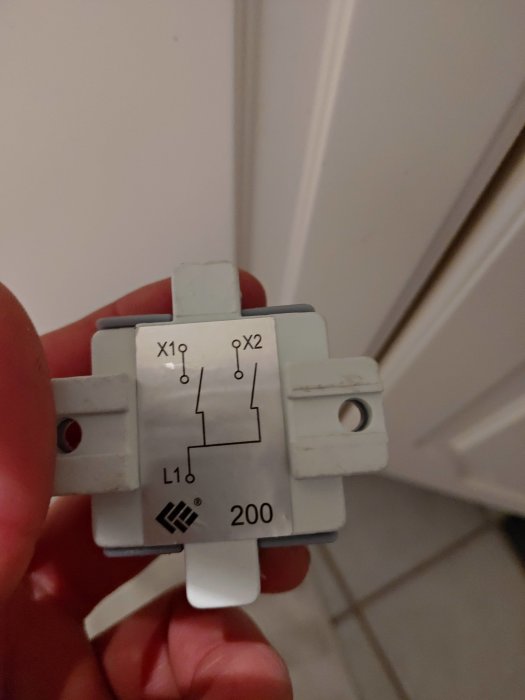 Närbild på en hand som håller en elektrisk brytare med schematiskt diagram och beteckningar.