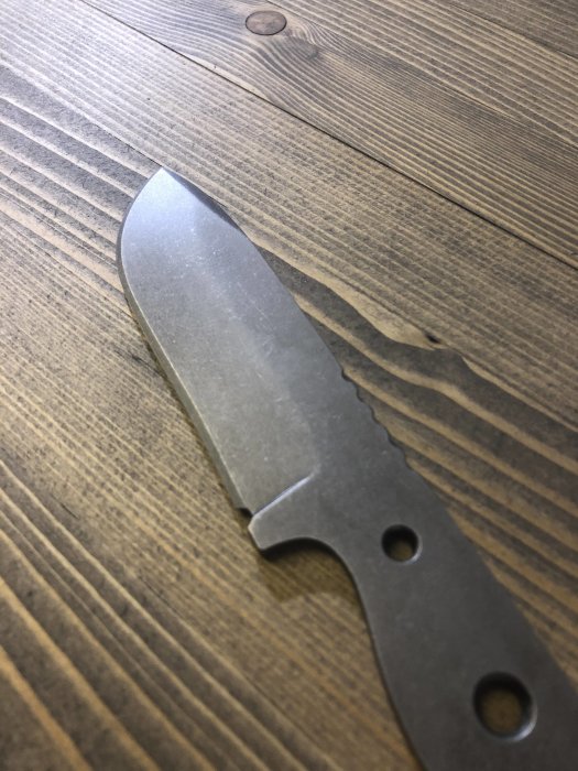 En hemgjord kniv i verktygsstål O2 ligger på ett träbord, ovässad och utan handtag.