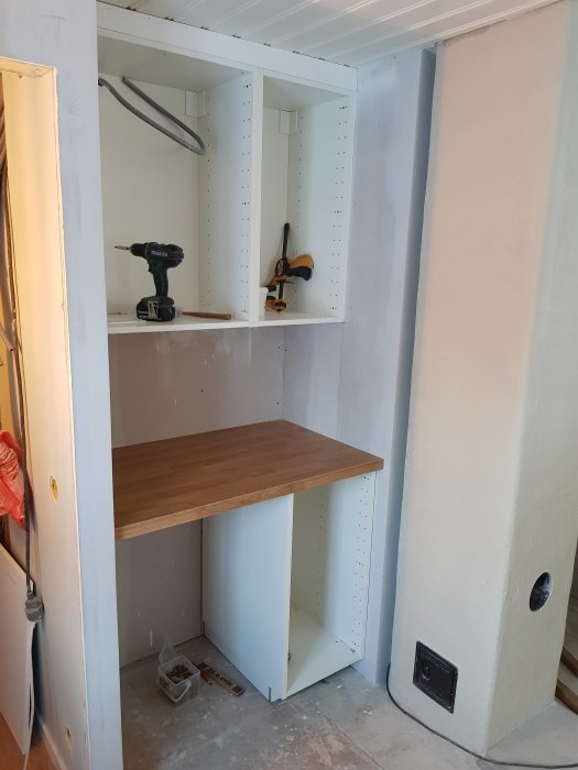 Nyinstallerade bänkskåp och bänkskiva i ett rum under renovering, utrymme för kylskåp under skivan.