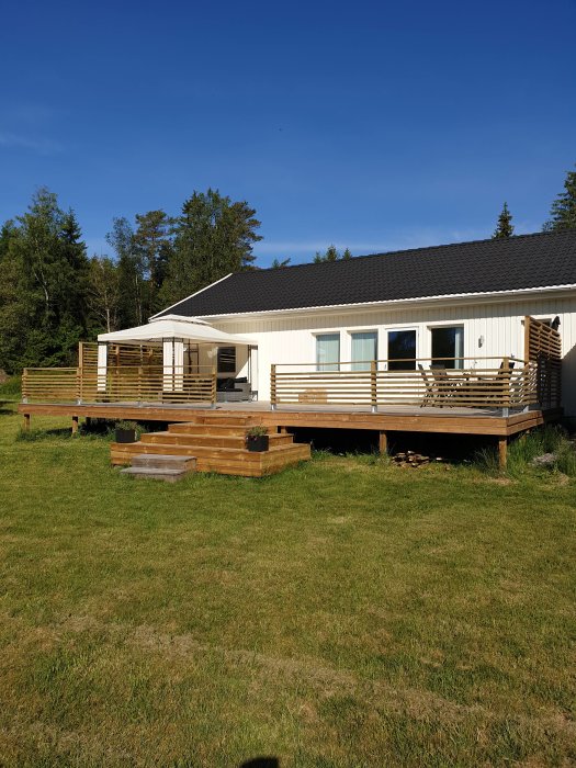 En vit villa med nybyggd terrass med räcken och integrerad trappa på en lutande tomt.