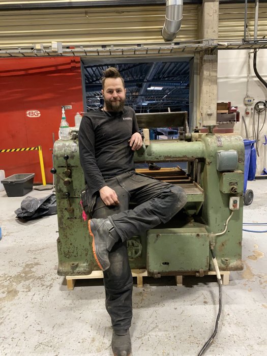 Person sitter på en äldre industriell maskin i en verkstad, signalerar maskinens kvalitet bortom lackskador.