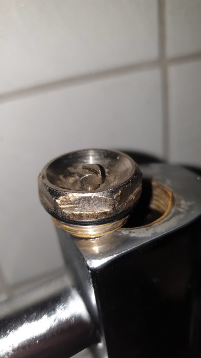Närbild på en avluftningsplugg på ett rör med synliga tätningstrådar och slitage.