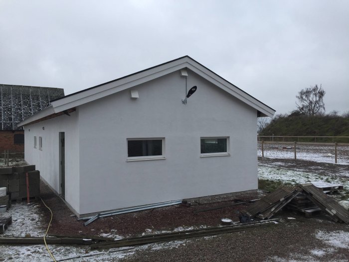 Vit snickeri verkstad med nyinstallerade vindskivor, en stor lampa, luftventil och snöfläckig mark.