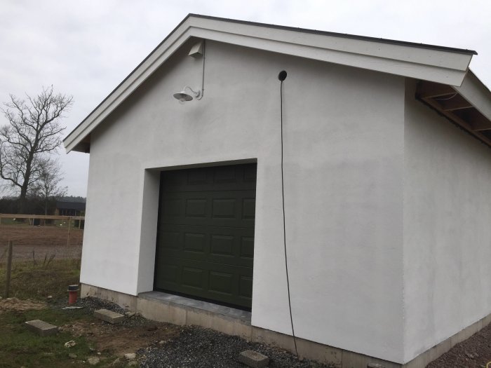 Vitputsad fasad på snickeriverkstad med nyinstallerad lampa och vindskiva, grön garageport.