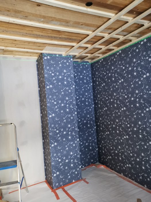 Pågående renovering med halvmonterade tapeter och exponerade takreglar i ett oavslutat rum.