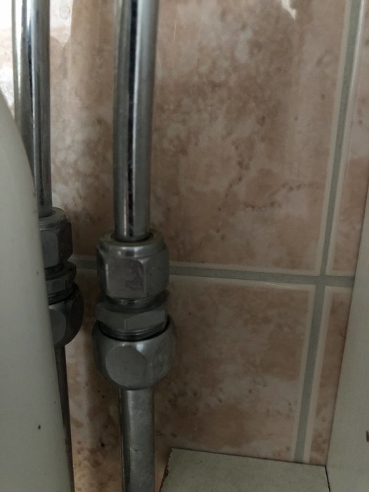 Närbild av gamla vattenrör med ovanlig 11 mm dimension i ett renoverat badrum, intill ett kaklat vägg.