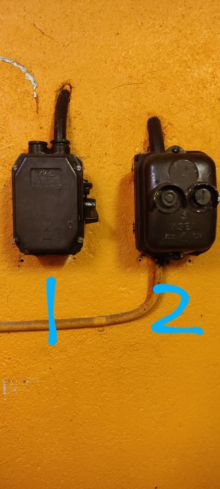 Två gamla strömbrytare på en orange vägg, märkta med siffrorna 1 och 2.