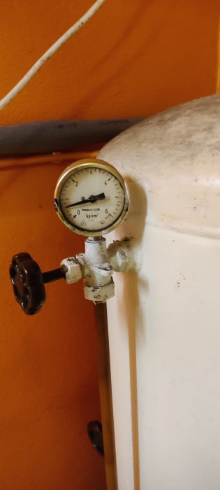 Tryckmätare på en vattenpump i en källare med hydrofor i bakgrunden, noll tryck visas.