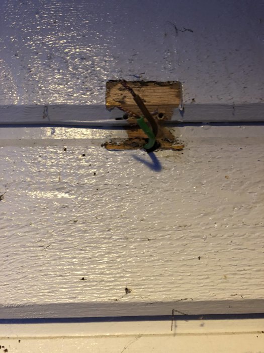 Två elektriska kablar (grön och brun) framträder ur en vägg där en kopplingsdosa tidigare suttit, märkt 2010.