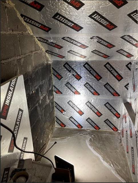 Ett utrymme under en trappa isolerat med silverfärgad isodrän-skiva och synliga betongväggar.