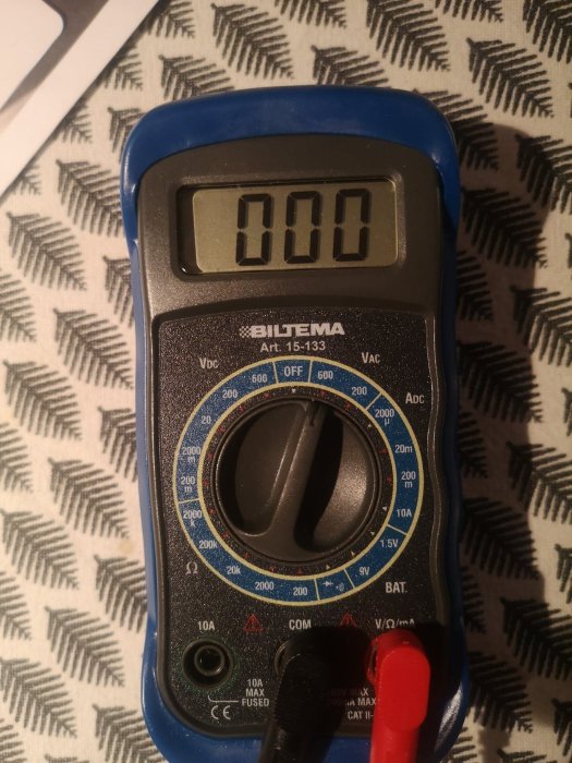 Multimeter inställd på VAC med en display som visar 0.00 och mätprober anslutna.