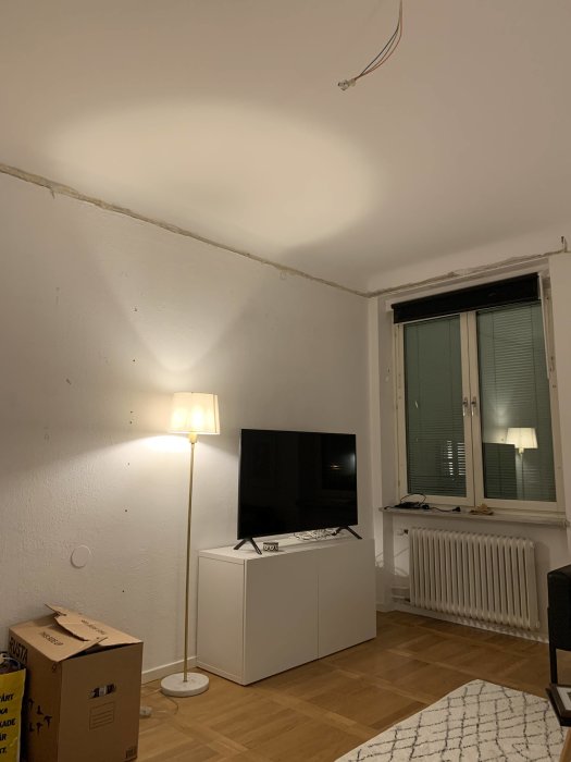 Nymålat vitt tak i rum med TV, golvlampa och osatt takrosett, med kommentar om att det är nästan färdigt.