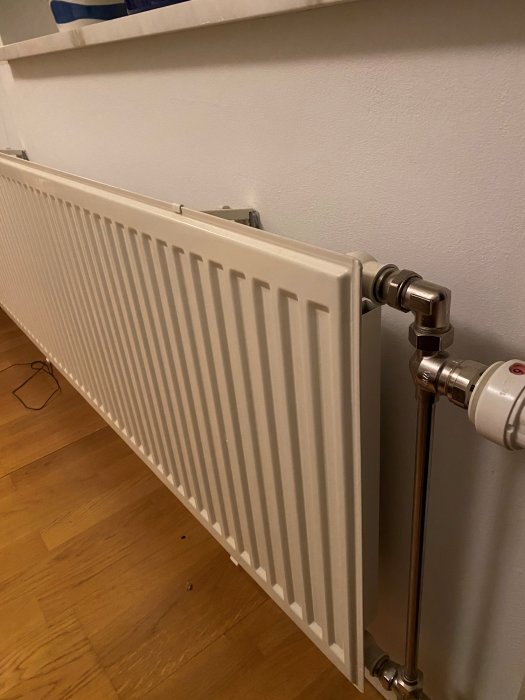 Vit plan radiator med termostatventil, installerad mot vägg i hus.