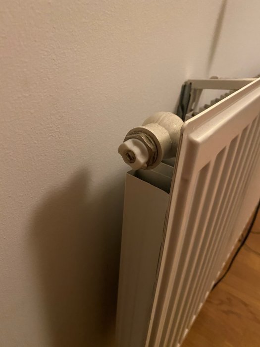 Vertikal vit radiator med termostatventil, installerad i ett hörn av rummet.