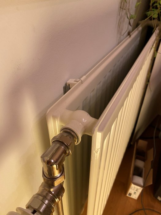 Vit radiator med termostat och anslutningsrör, installerad intill en vägg, efterfrågas identifiering.