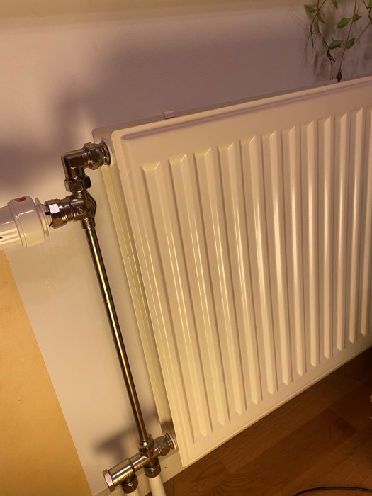 Vit radiator med anslutna ventiler och rör, monterad på väggen, från 2004.
