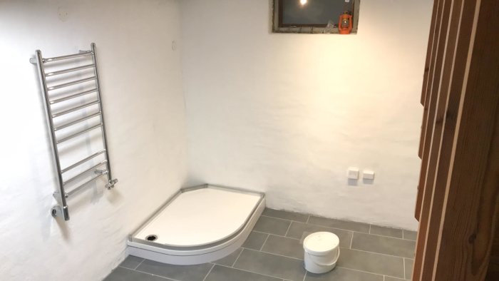 Renoverat badrum med duschhörna, toalett och handdukstork på vitmålad vägg.