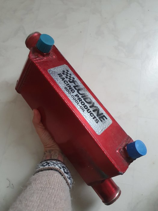 Hand håller en röd racerbilshydraulisk domkraft med blåa skyddslock.