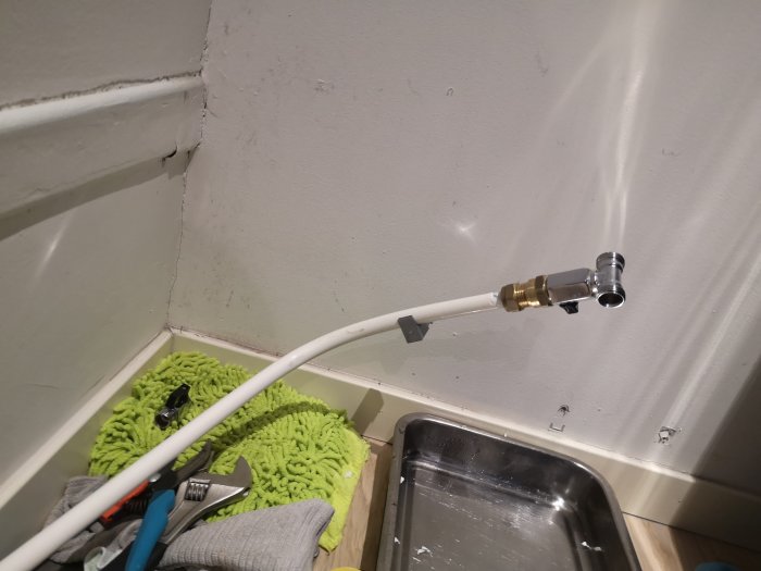 Vit vattenledning med kopplingar nära en diskbänk och verktyg på en grön matta.