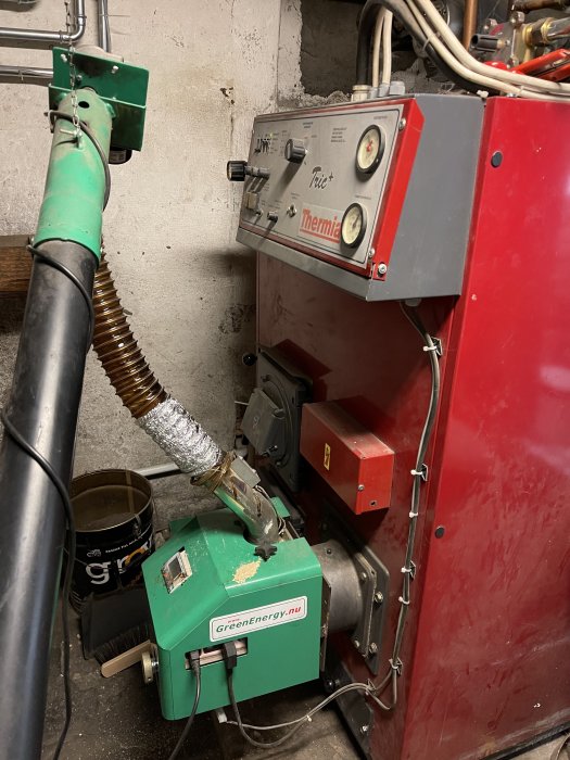 En Green Energy P20 pelletsbrännare i ett pannrum med synliga rör och kablar, samt användarkontrollpanel.