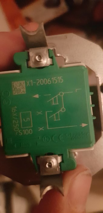 Närbild av en grön elektrisk komponent med märkningen 'Schneider Electric' och symboler för elektrisk anslutning.