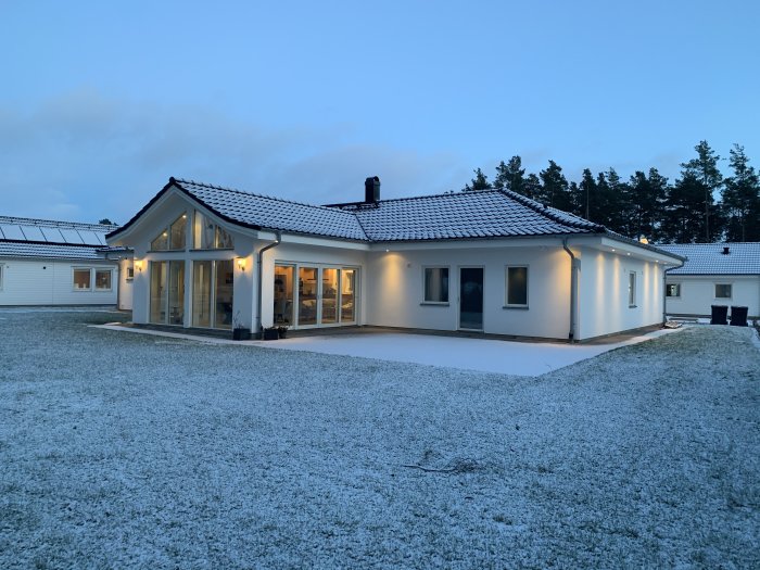 Ett modernt enfamiljshus täckt av ett tunt lager snö i skymningen.