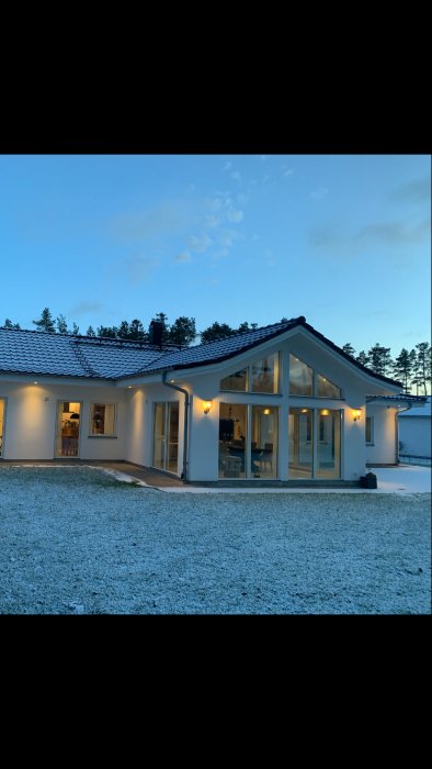 Ett modernt hus med tända lampor i skymningen och ett lätt lager av snö på gräsmattan.