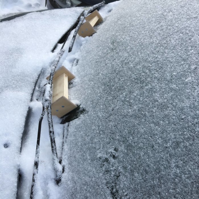 Vindruta på en bil med isiga torkarblad och träklossar som lyfter dem från glaset.