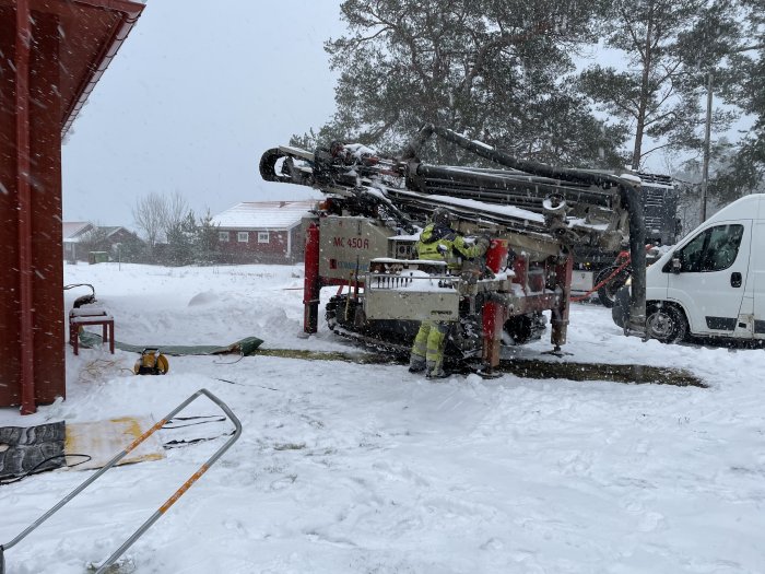 Arbetsfordon och personal i snölandskap tar bort utomhusenhet till en luft/vatten-pump.