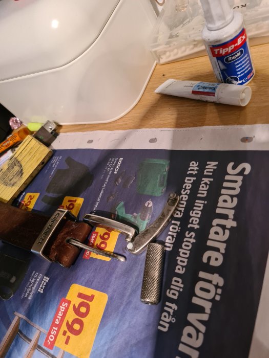 Ett trasigt bältesspänne och ett brunt läderbälte på en tidning med limtuber i bakgrunden.