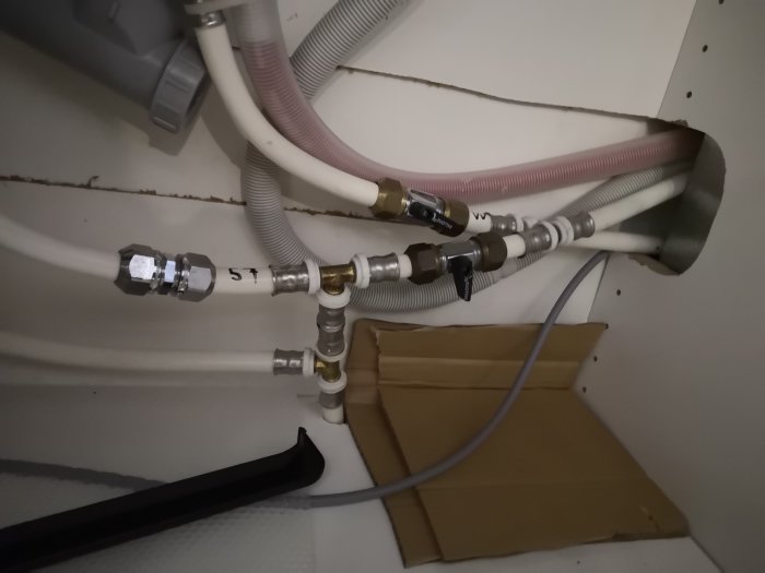 Rörinstallation under ett skåp med olika kopplingar och slangar som visar den beskrivna problematiken.