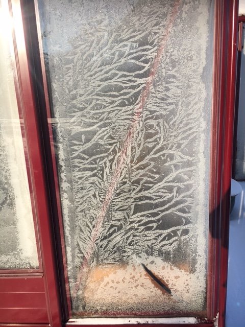 Isfönster med naturligt mönster av frost på en kall dag.