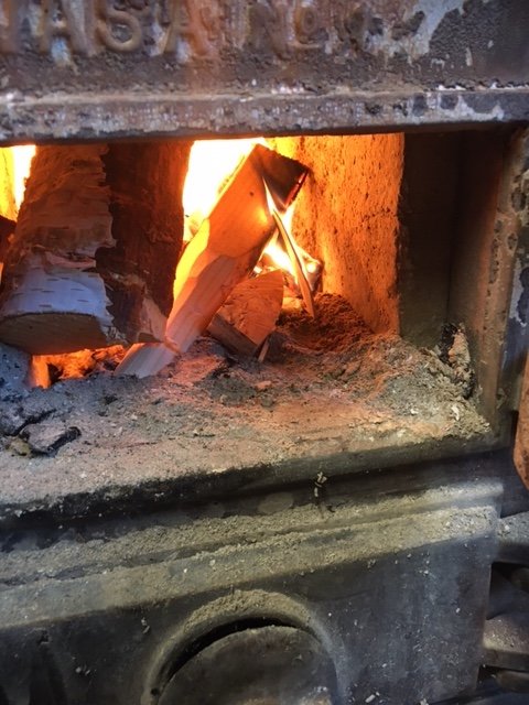 Gammal kamin med eld och ved inuti, används för att värma verkstaden.