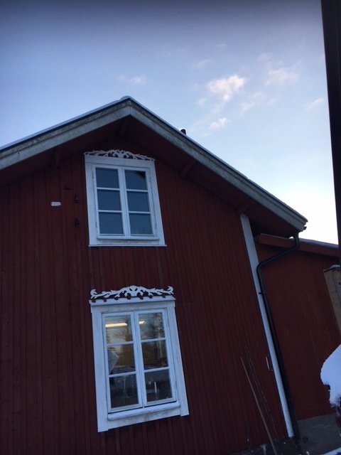 Frostiga mönster på röd träverkstadsfasad med vita fönster och snö på fönsterblecket.