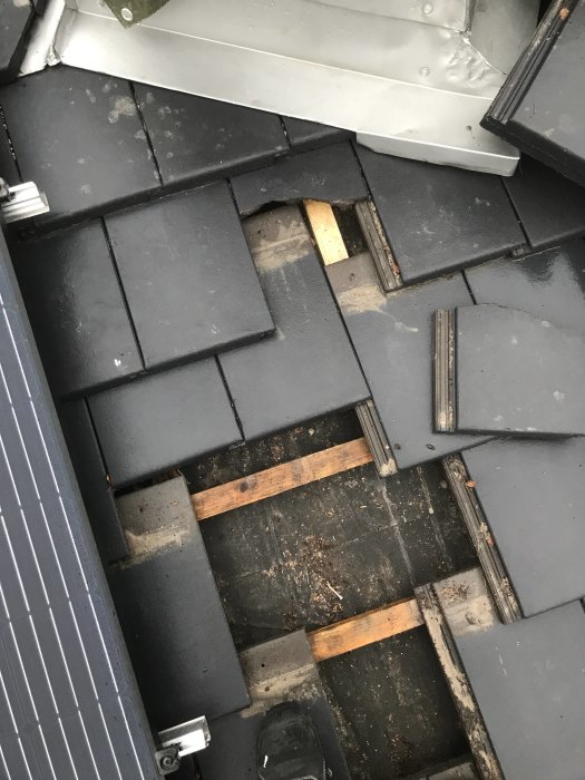 Skadade svarta takpannor från Benders med synlig läkt och underlag, beskrivning av problem med taksystemet.