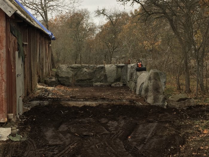 Gammal gödselstack med stora stenar bredvid lada, tänkt som grund för garagebygge.