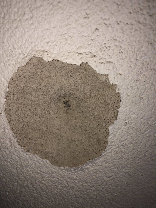 Söndervittrad puts runt skruv i betongvägg, misstänkt fuktskada nära badrumsfäste.