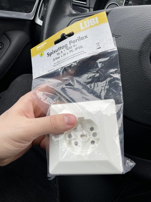 Hand håller ett nytt Perilex spisuttag mot en bilratt, förberedelse för installation.