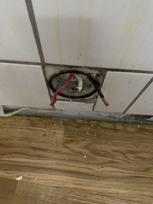 Öppen elanslutning med tre ledningar på ett klinkergolv vid en vägg, redo för installation av perilexuttag.