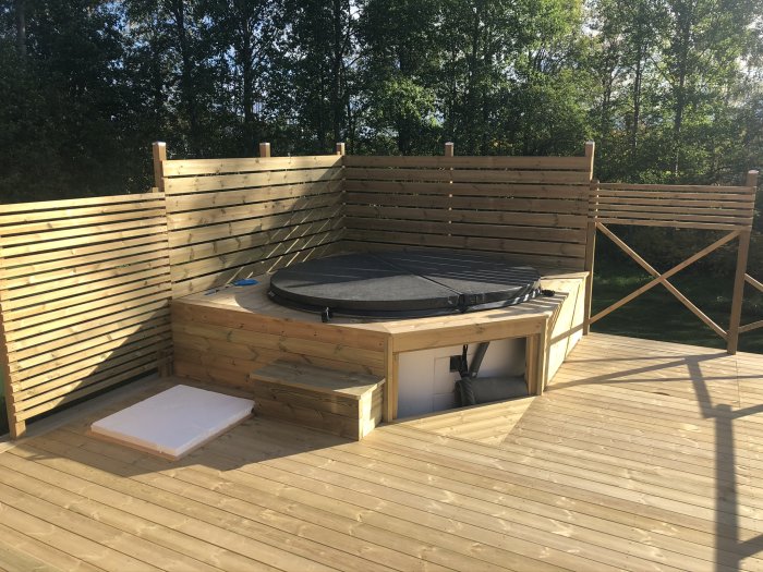 Träterrass med nyinstallerad rund terasspool och täcklock, omgärdad av trästaket med skog i bakgrunden.