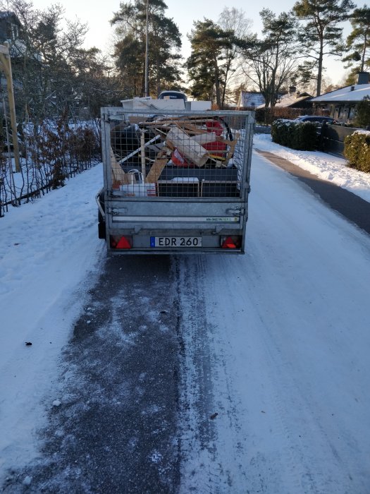 Lastad släpvagn med byggmaterial på en snöig väg.