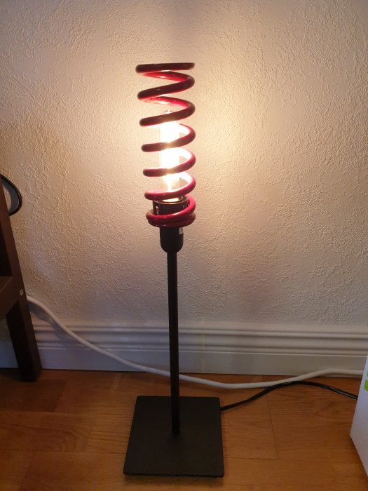 3D-utskriven adapter som förbinder en spiralformad fjäder med en lampsockel, agerande som en ovanlig lampskärm.