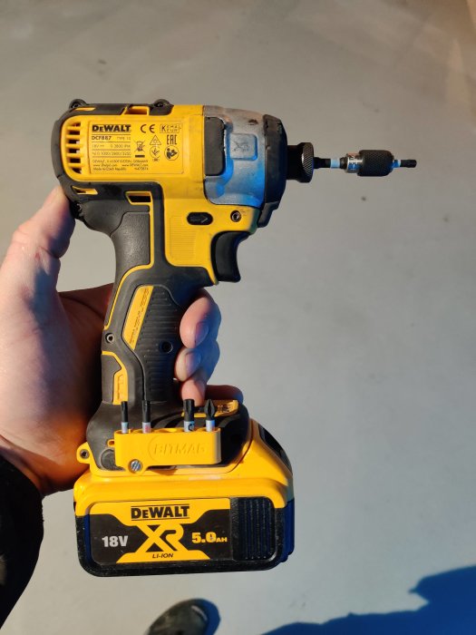 Hand håller en DeWalt borr med ett batteri och en Bitmag bitshållare fäst vid basen.