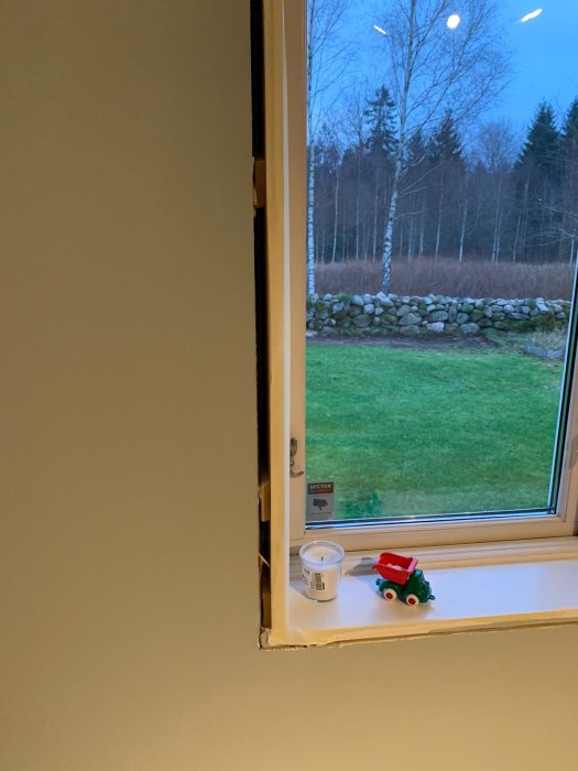 Utsikt genom ett fönster utan foder med synlig distanskloss och tumstock för mätning.