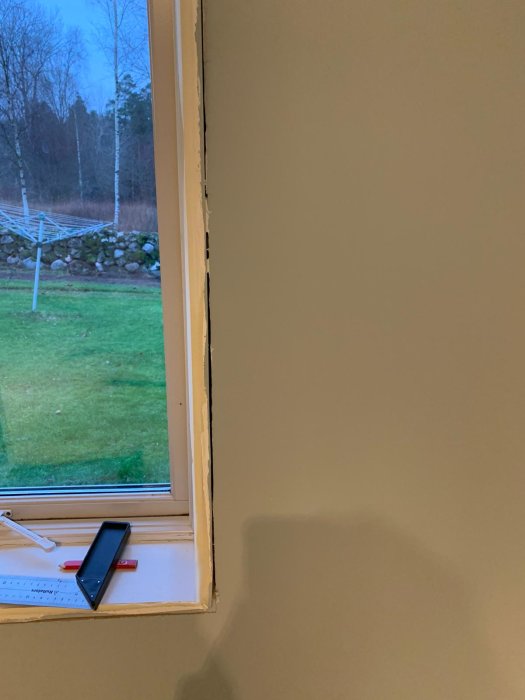 Renoverat rum med borttaget fönsterfoder som visar isolering och en tumstock på fönsterbrädan.